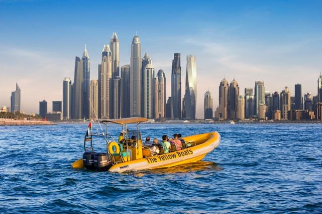 Yellow boat with passengers on water, skyscrapers in the background.